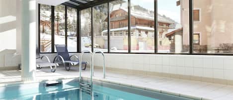 A swimming pool with a glass enclosure, a metal ladder, and lounge chairs.