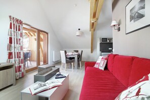 Ein gemütliches Wohnzimmer mit einem roten Sofa, einem Essbereich mit Tisch und Stühlen sowie einer Küchenzeile mit einer Mikrowelle.