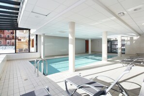 Ein Poolbereich mit gefliestem Boden, Metallleiter und Liegestühlen.