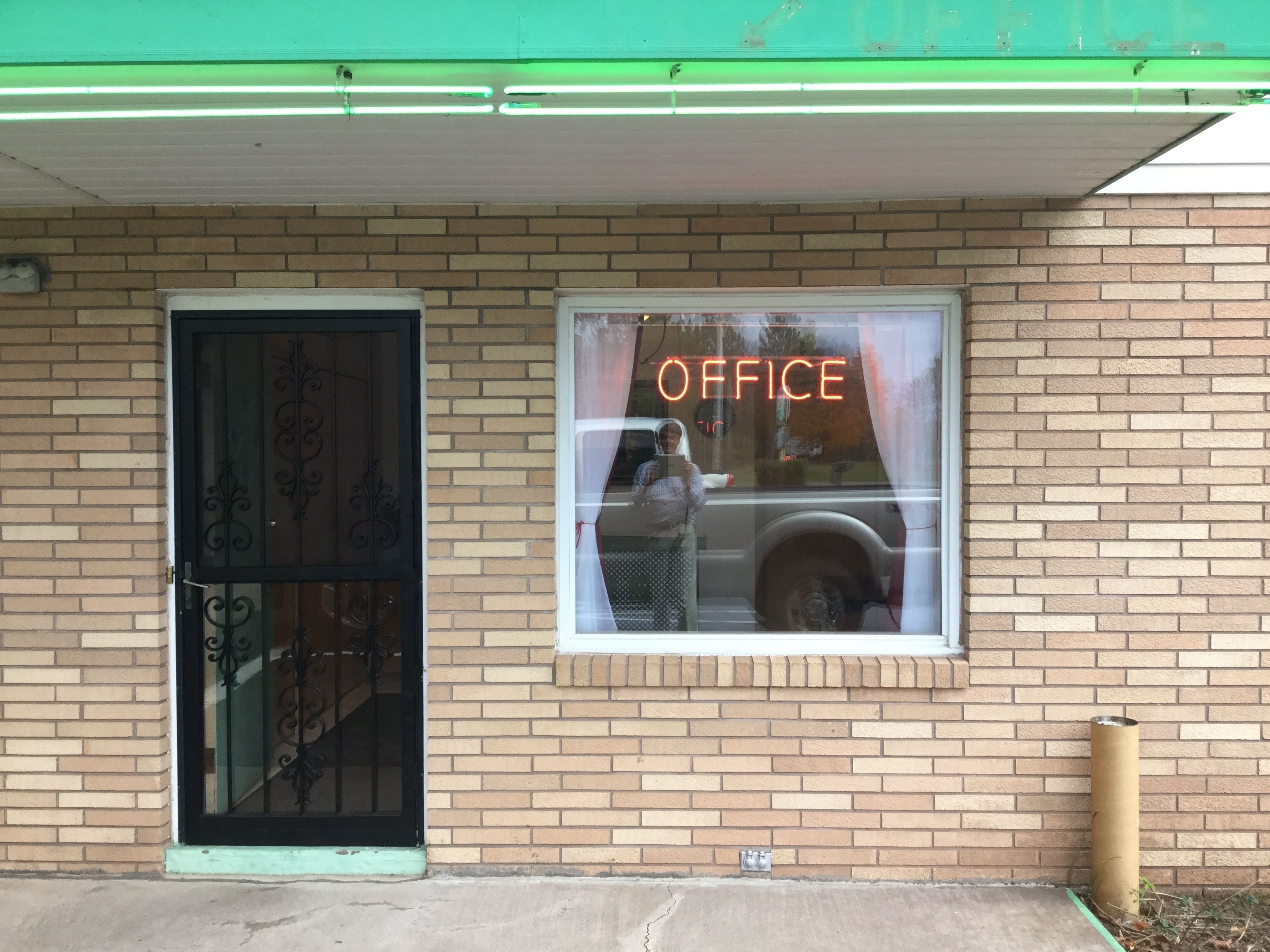 A building with a brick facade, a black metal door, and a window with the word "OFFICE" illuminated.