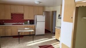 Una cocina compacta con armarios de madera, un refrigerador, una cafetera y una mesita.