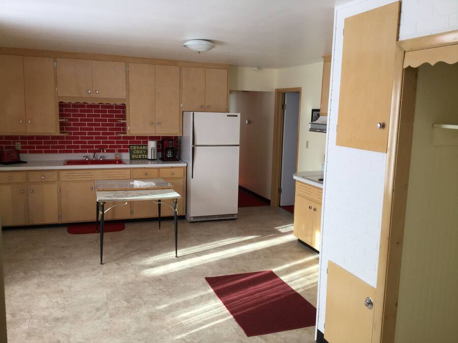 A compact kitchen with wooden cabinets, a refrigerator, a coffee maker, and a small table.