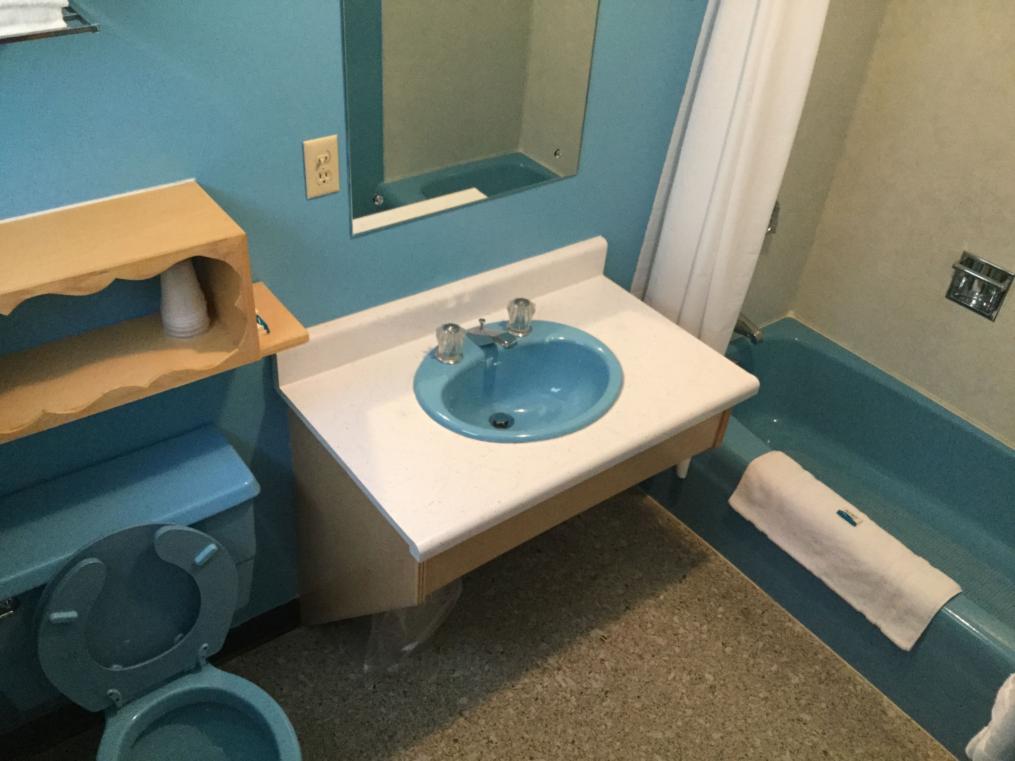 Un baño con un lavabo azul, un inodoro y un espejo.