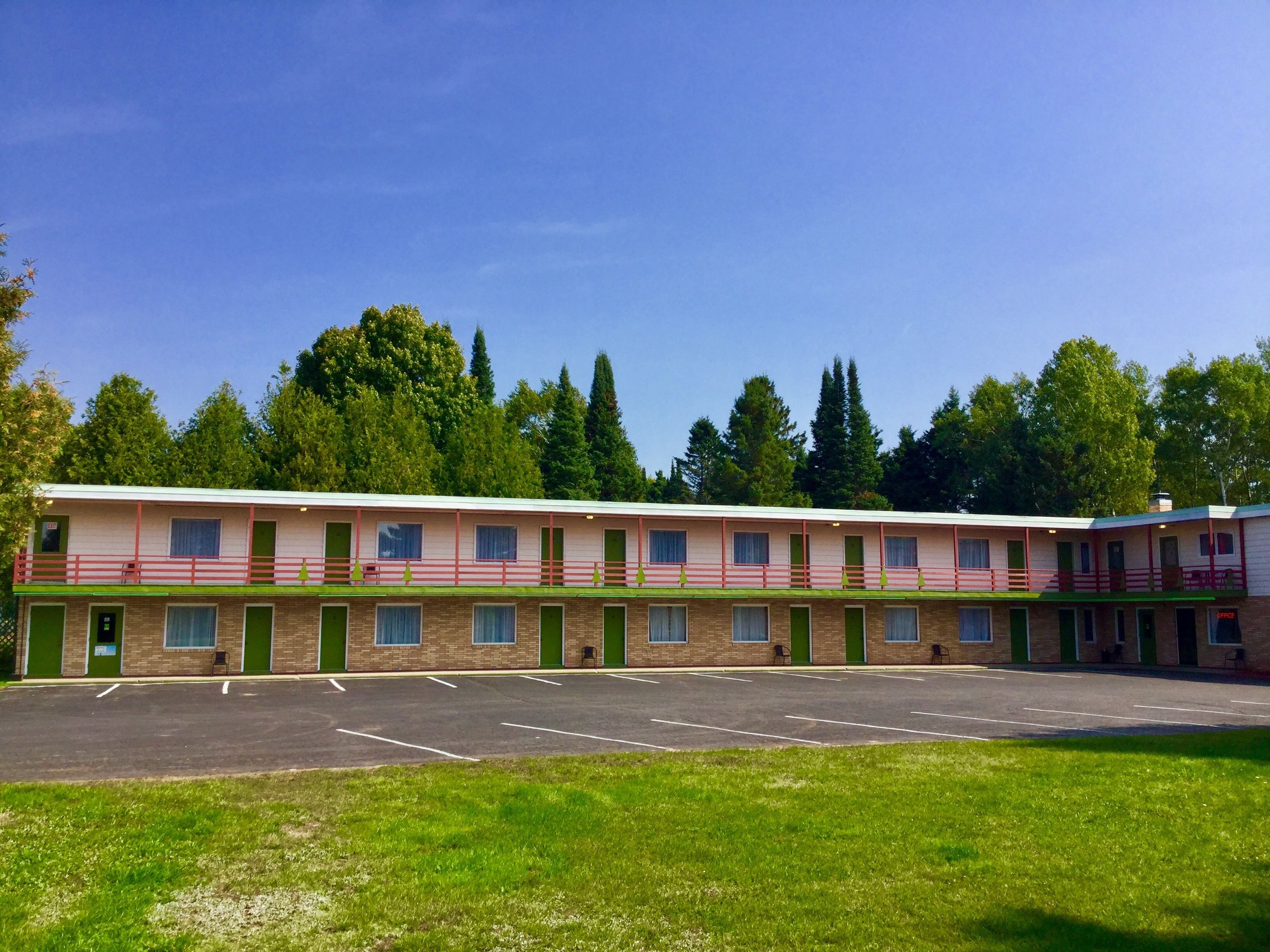 A motel with a row of rooms, a parking lot, and a grassy area in front.