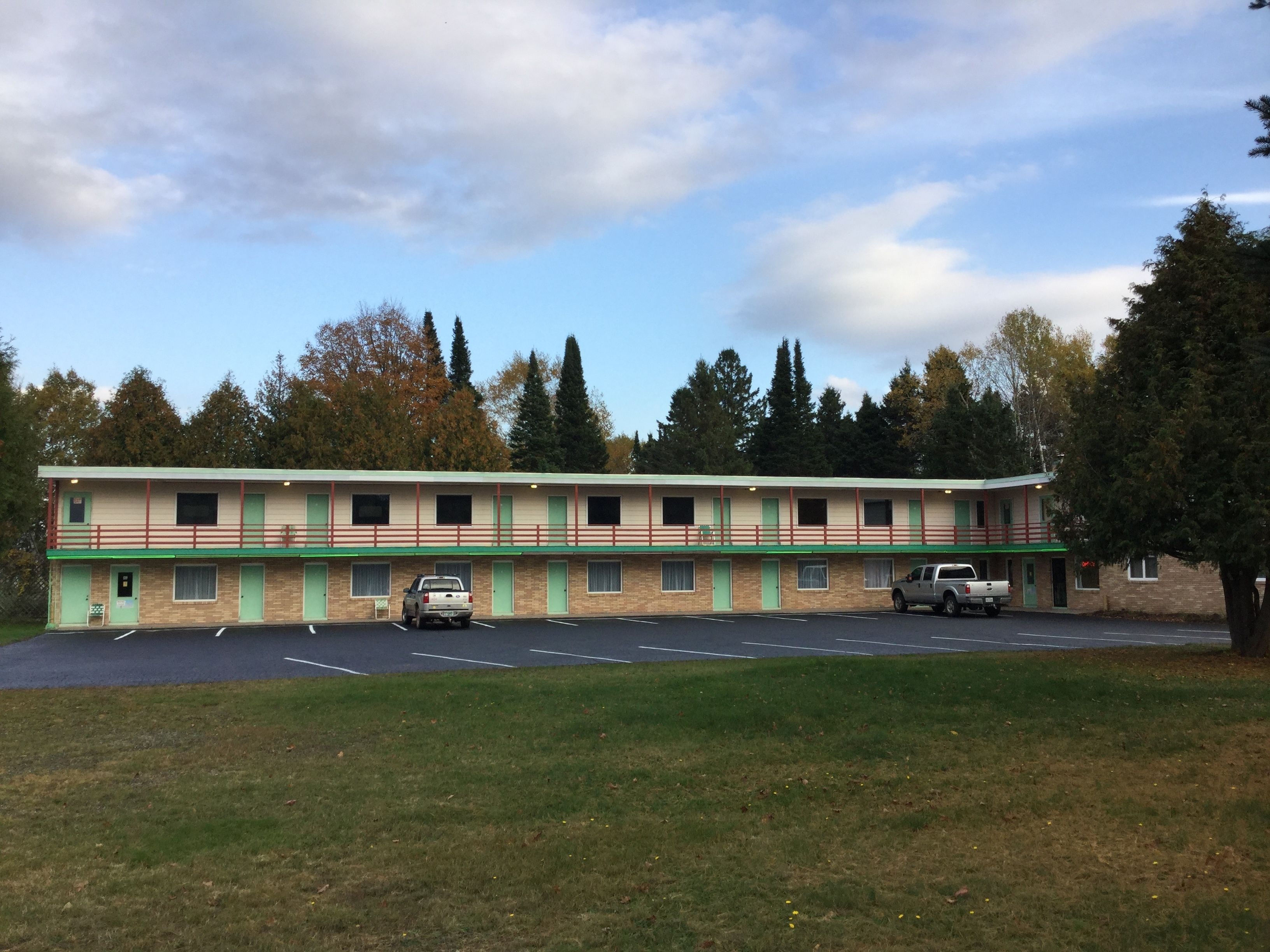 A motel with a two-story structure, a parking lot, and a grassy area in front.
