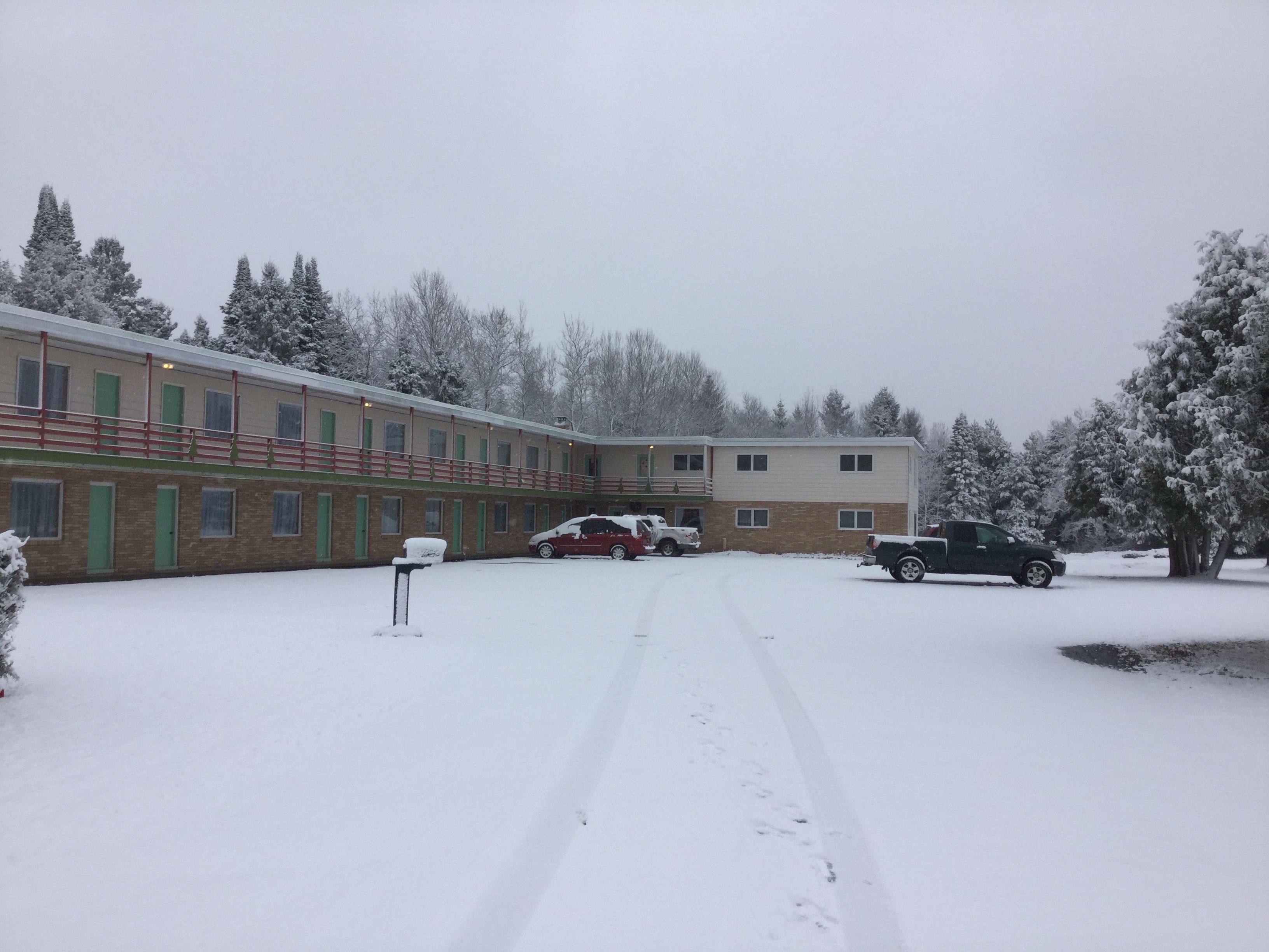 Ein zweistöckiges Gebäude mit Backsteinfassade und grünen Türen, umgeben von schneebedeckten Bäumen.