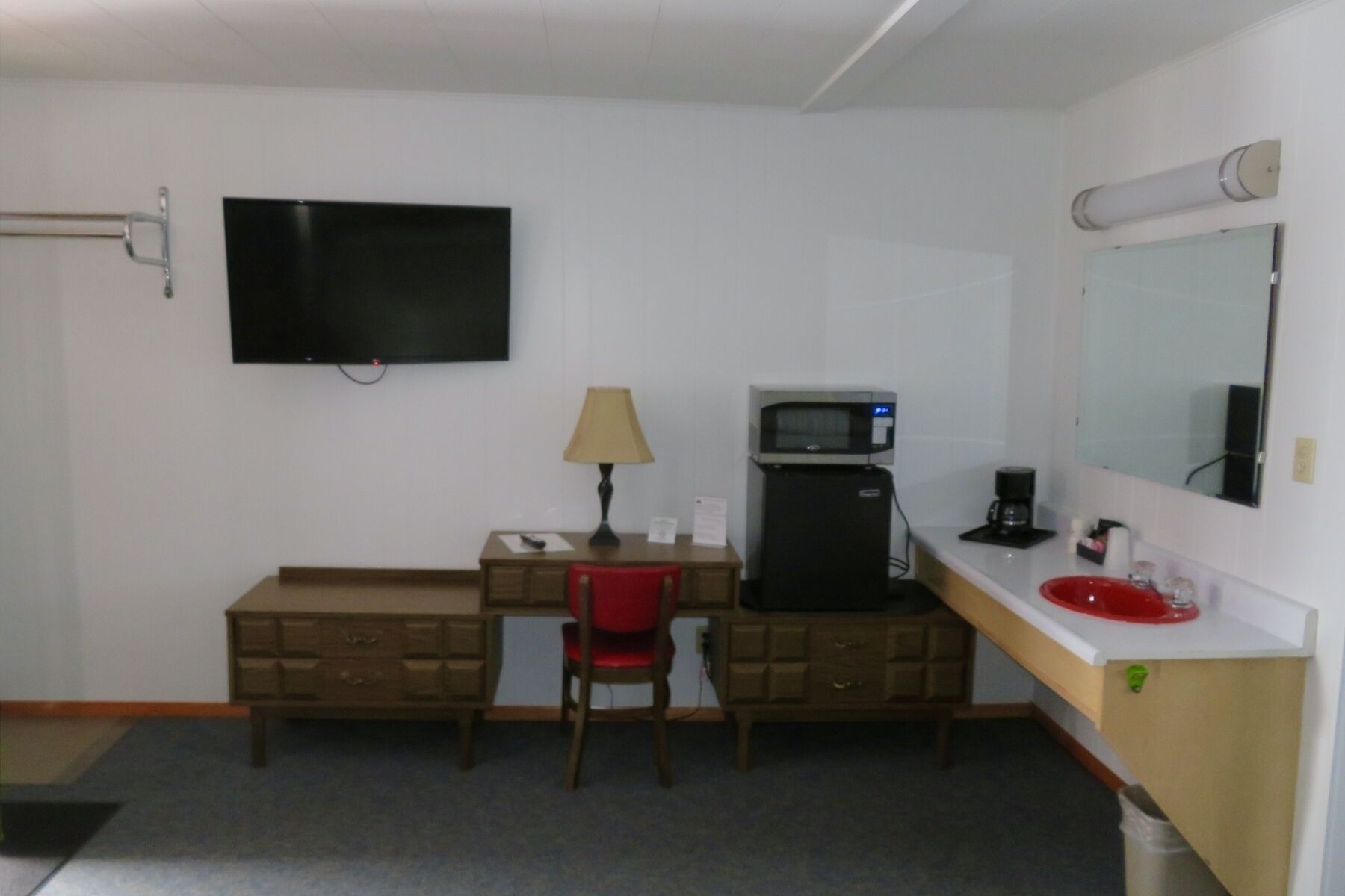 Ein Hotelzimmer mit Flachbildfernseher, Schreibtisch mit Lampe, Mikrowelle, Kaffeemaschine und einem roten Waschbecken.