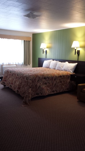A hotel room with a large bed, two bedside lamps, a headboard, and a window with curtains. - Cedars Motel (Ironwood)