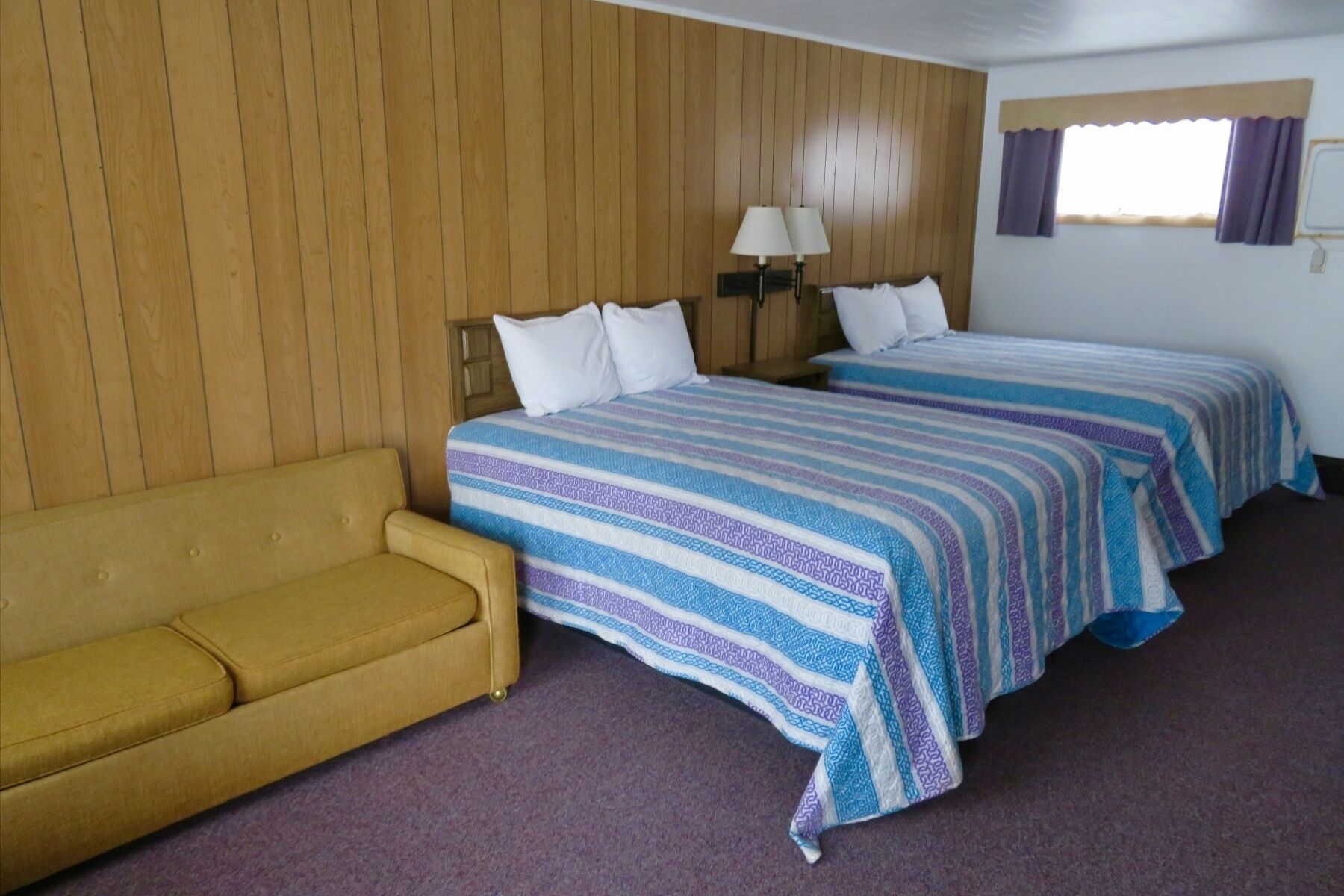 A room with two beds, a sofa, and a window with curtains.
