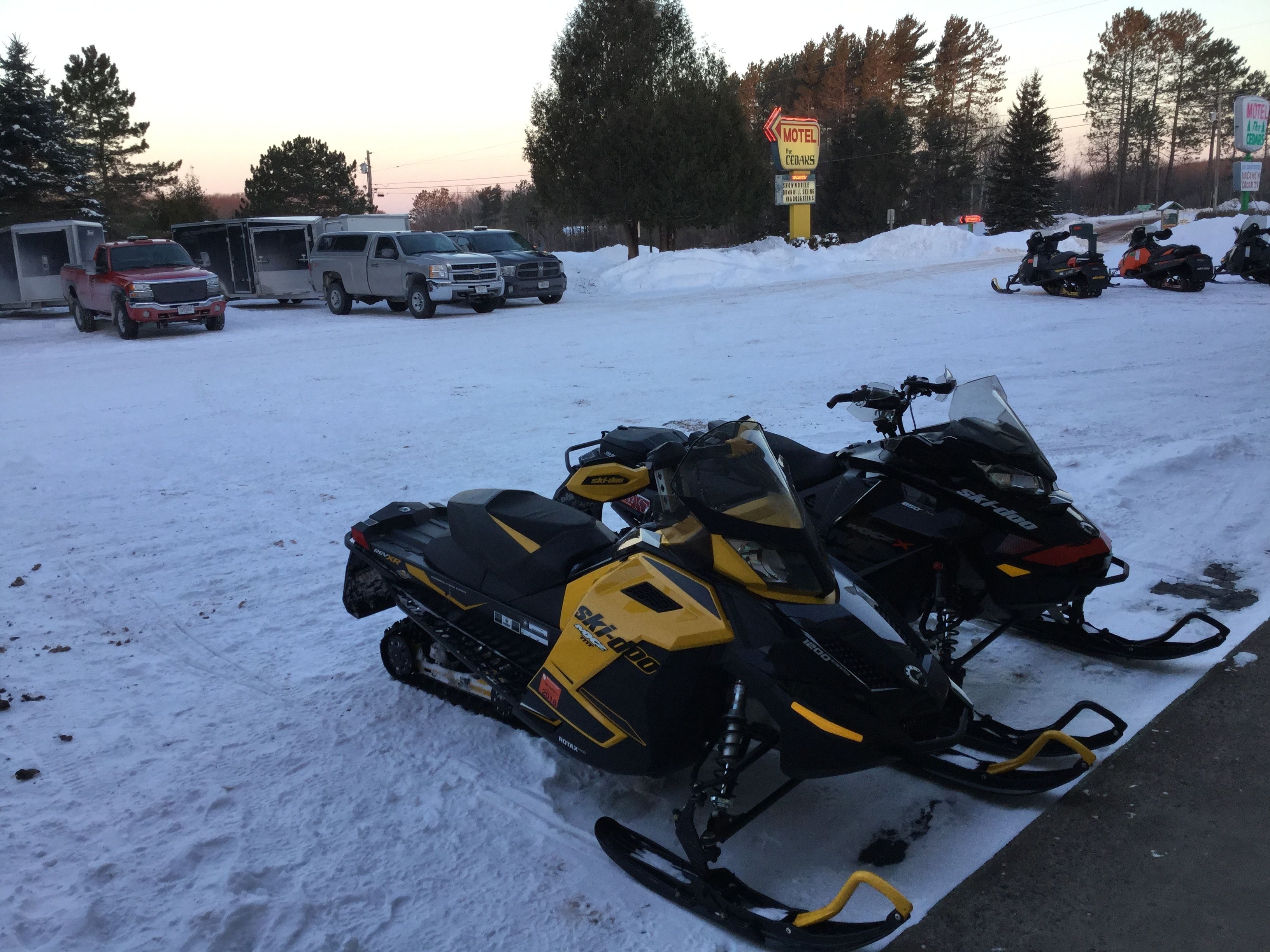 Zona de estacionamiento para motos de nieve con un letrero de motel al fondo.