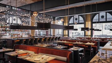 Un interior de restaurante moderno con techos altos, paredes de ladrillo visto y diversas opciones de asientos, incluyendo cabinas y mesas.