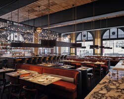 A modern restaurant interior with high ceilings, exposed brick walls, and a variety of seating options including booths and tables.