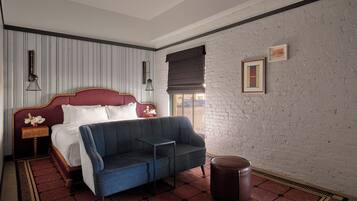 A hotel room with a bed, a blue sofa, a small table, a round ottoman, and a window with a view.