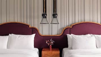A double bed with white linens, a wooden nightstand with a vase, and two wall-mounted lamps.