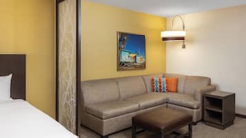 A hotel room with a bed, a sofa, a small table, a nightstand, and a painting on the wall.