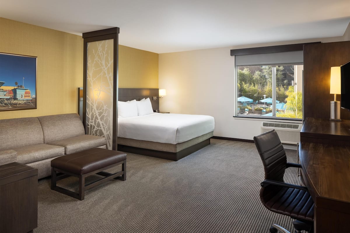 Habitación de hotel con cama, sofá, escritorio y vistas al exterior.