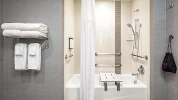 A modern bathroom with a bathtub, shower, and handrails.