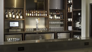 A bar area with wooden beams, hanging pendant lights, a wine display, and bar stools. - Hyatt Place Santa Cruz (Santa Cruz)