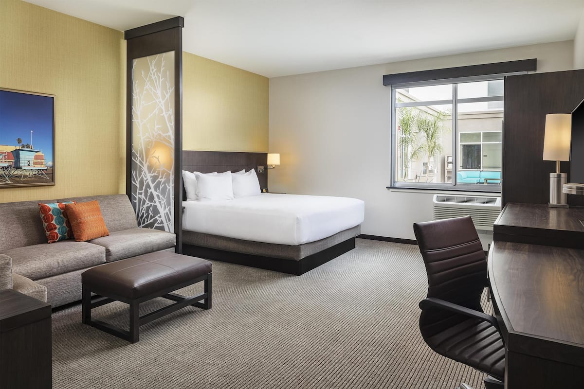 Habitación de hotel con cama, sofá, escritorio y ventana con vista a la piscina.