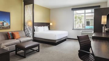 Ett hotellrum med en säng, en soffa, ett skrivbord och ett fönster med utsikt över en pool.