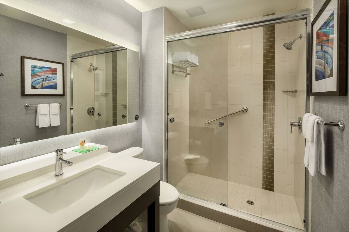 A modern bathroom with a large mirror, two sinks, a shower, and a toilet.