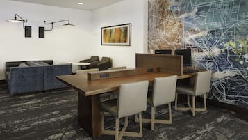 A modern office space with a long wooden table, four chairs, a sofa, and two wall-mounted lamps.