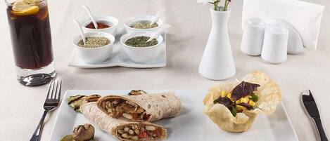 Un repas comprenant une boisson, une assiette avec un burrito et une salade, ainsi que des condiments sur la table.