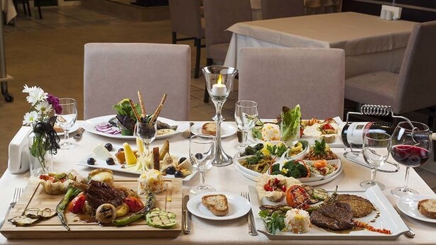 A dining table set with various dishes and wine glasses, surrounded by chairs in a restaurant setting. - Hotels Dalgiclar (Corum)