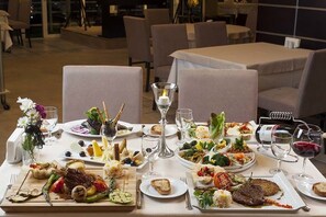 Una mesa de comedor dispuesta con diversos platos y copas de vino, rodeada de sillas en un ambiente de restaurante.