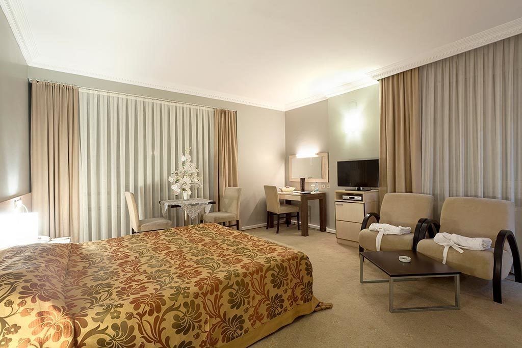 A hotel room with a large bed, a desk, a television, and two armchairs.