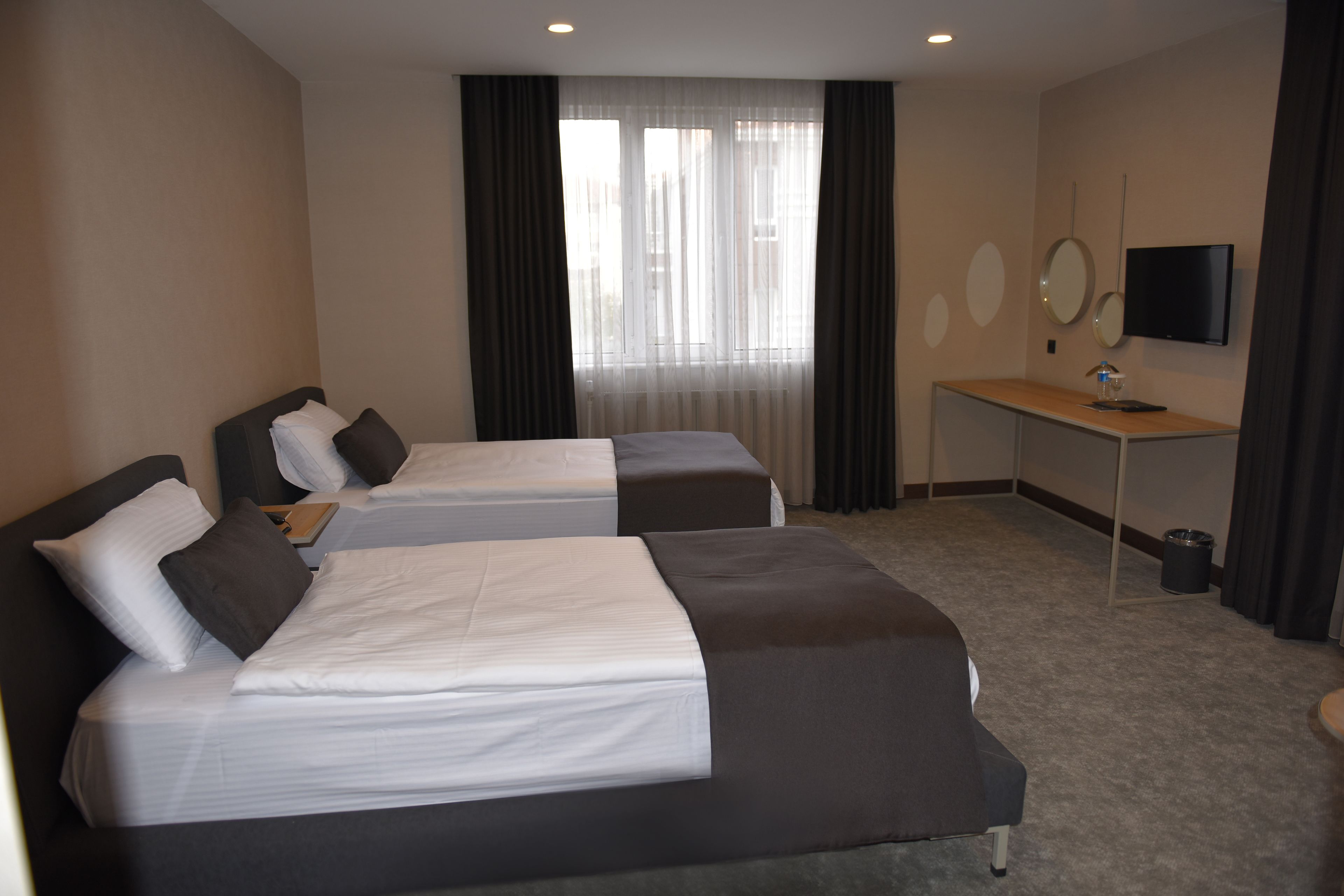 A hotel room with two beds, a desk, a TV, and a window with curtains.