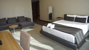 A modern hotel room with a large bed, a sofa, a small table, and a mirror. - Hotels Dalgiclar (Corum)