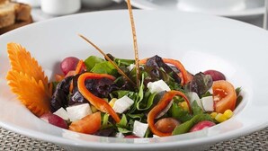 A white plate with a colorful salad, including greens, carrots, and cheese, garnished with a carrot flower and two sticks. - Hotels Dalgiclar (Corum)