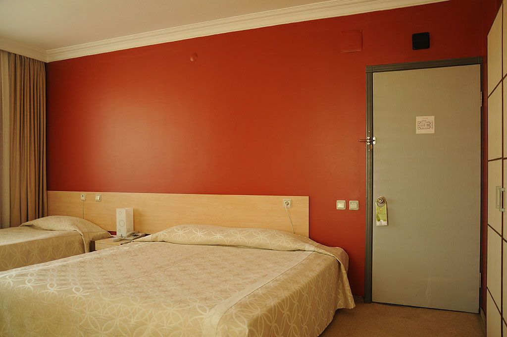 Une chambre d’hôtel avec deux lits, une tête de lit en bois, une porte avec une pancarte et un rideau sur le côté gauche.