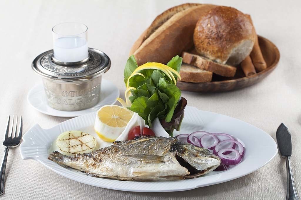 A plate with grilled fish, lemon, and salad, accompanied by bread and a candle.