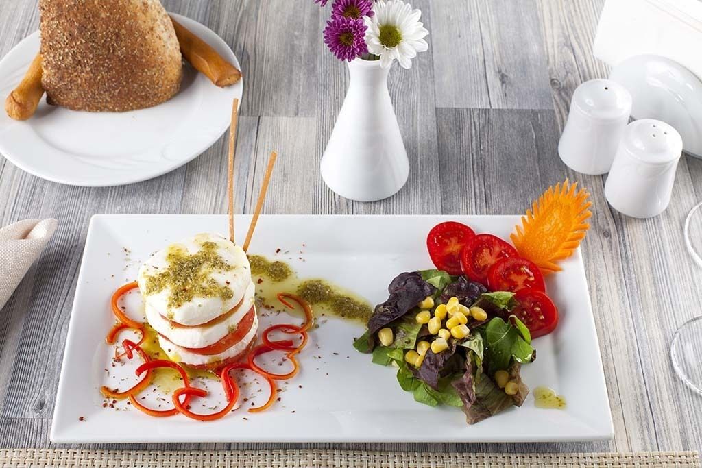 A plate with mozzarella balls, a salad, and breadsticks on a wooden table.