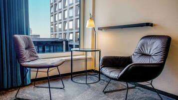 Habitación de hotel con dos sillones de cuero, una mesita, una lámpara de pie y vistas a un edificio a través de una ventana.
