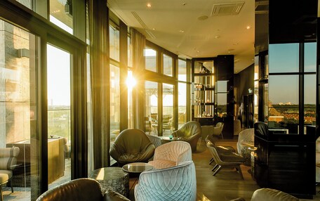 A spacious lounge area with leather sofas, a round table, and a view of the cityscape through large windows.