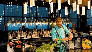 Un bar où un barman prépare des boissons, avec des étagères remplies de bouteilles et un saladier rempli de citrons.