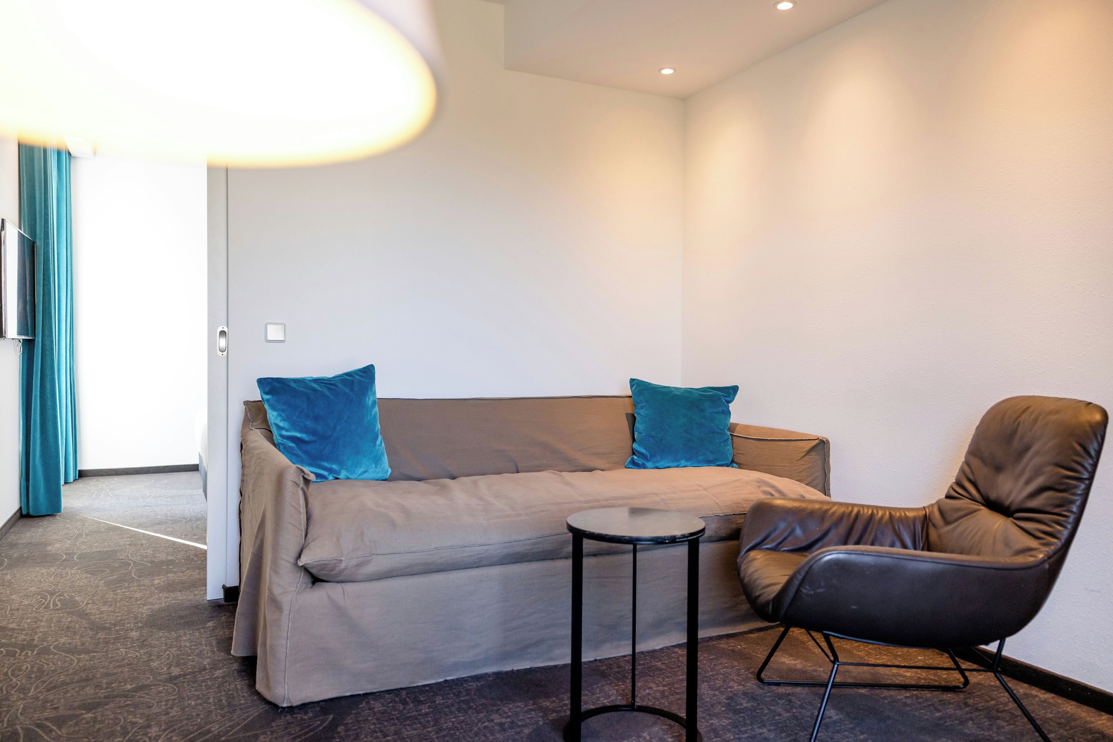 Ein modernes Zimmer mit einer Couch, zwei Kissen, einem kleinen Tisch und einem Ledersessel.