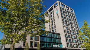 Un bâtiment d'hôtel moderne, avec une enseigne « Motel One » bien visible, de grandes fenêtres et un arbre au premier plan.