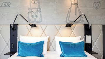A hotel room with a modern design, featuring a bed with white bedding and blue pillows, two black nightstands, and a wall with a circuit board pattern.