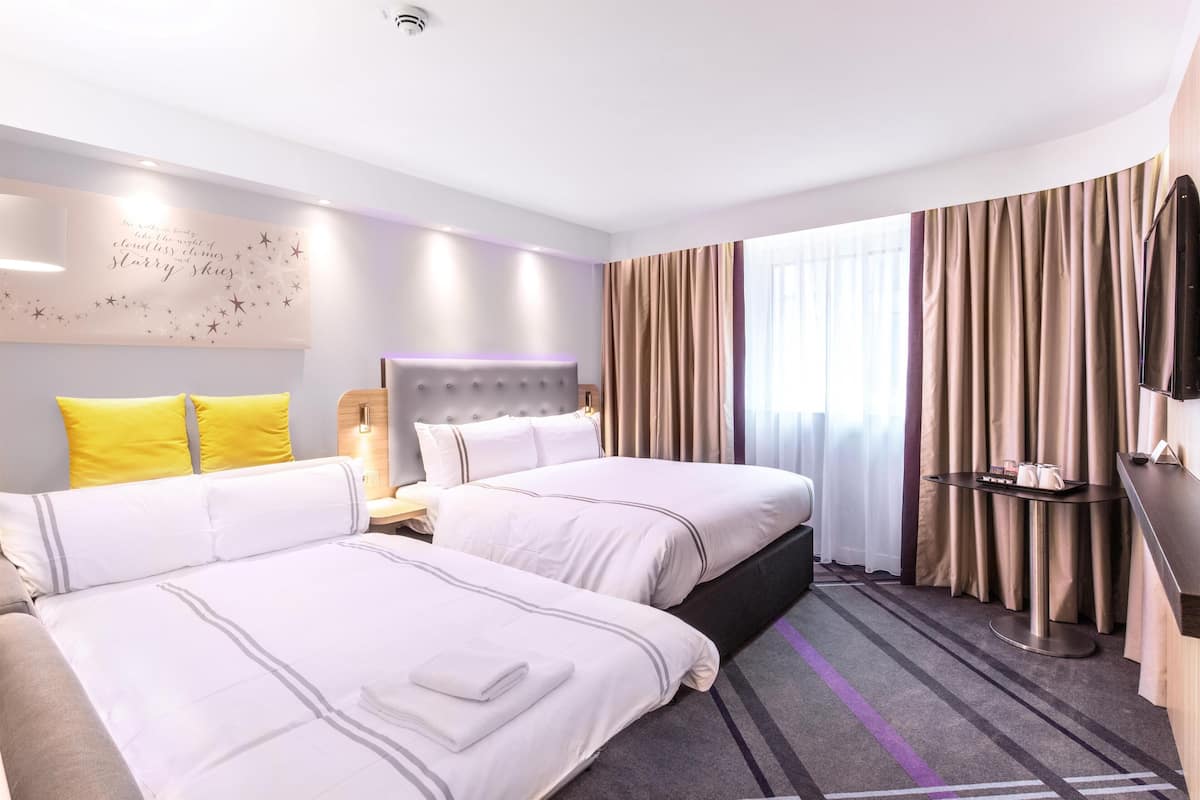 Habitación de hotel con dos camas, un televisor de pantalla plana, una mesita de noche y un ventanal con cortinas.