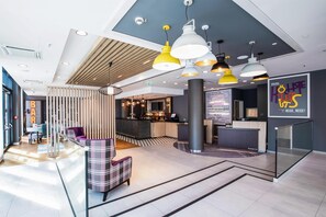 Eine moderne Hotelhalle mit Empfangsschalter, Barbereich und Sitzgelegenheiten.