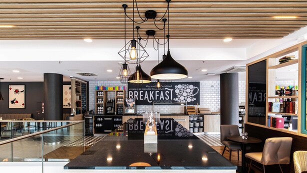 Un área de cocina moderna con una isla central, iluminación colgante y un cartel que dice 'BREAKFAST'.