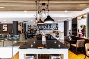 A modern kitchen area with a central island, pendant lighting, and a visible sign that reads 'BREAKFAST.' - Premier Inn Hamburg City Hammerbrook (Hamburg)