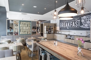 A modern breakfast area with seating, a kitchen counter, and a wall with a quote. - Premier Inn Freiburg City Süd (Freiburg im Breisgau)