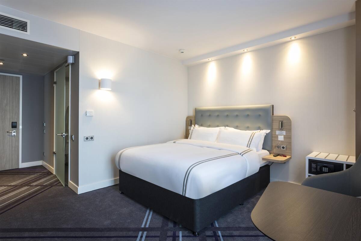 Une chambre d’hôtel moderne, dotée d’un grand lit, de tables de chevet, d’un bureau et d’une chaise.