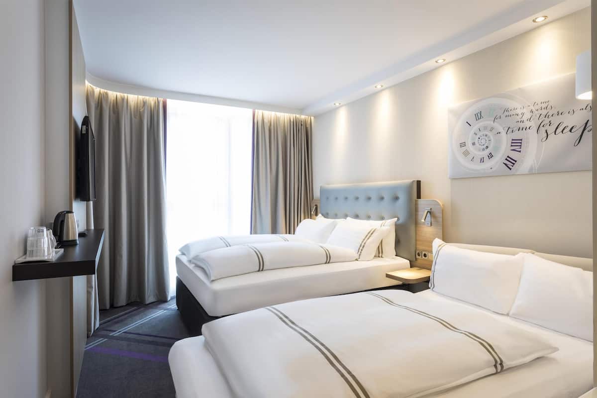 Une chambre d’hôtel avec deux lits, une télévision, une horloge et une fenêtre avec des rideaux.