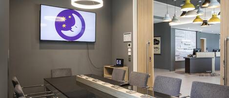 A conference room with a long table, chairs, a TV, and a reception desk in the background.
